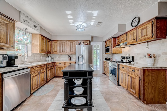 kitchen featuring decorative backsplash, a textured ceiling, stainless steel appliances, light tile patterned floors, and a center island