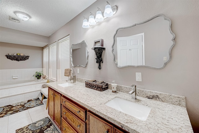 bathroom with tiled bath, tile patterned flooring, vanity, and a textured ceiling