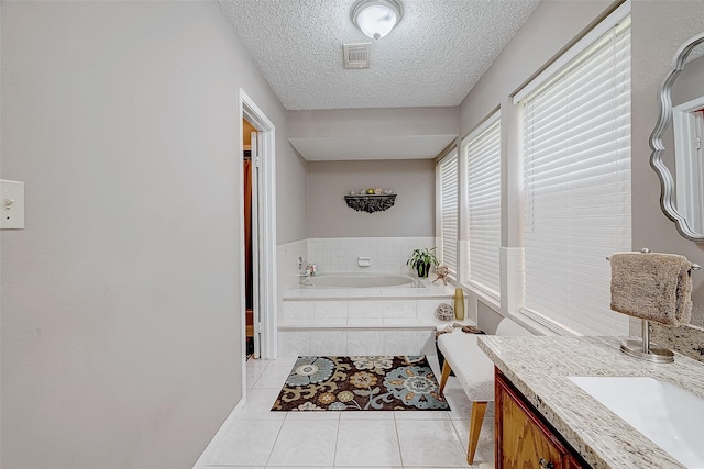 bathroom with tile patterned floors, vanity, a textured ceiling, and tiled tub