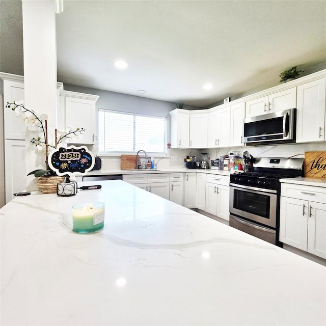 kitchen with light stone countertops, stainless steel appliances, decorative backsplash, white cabinetry, and sink