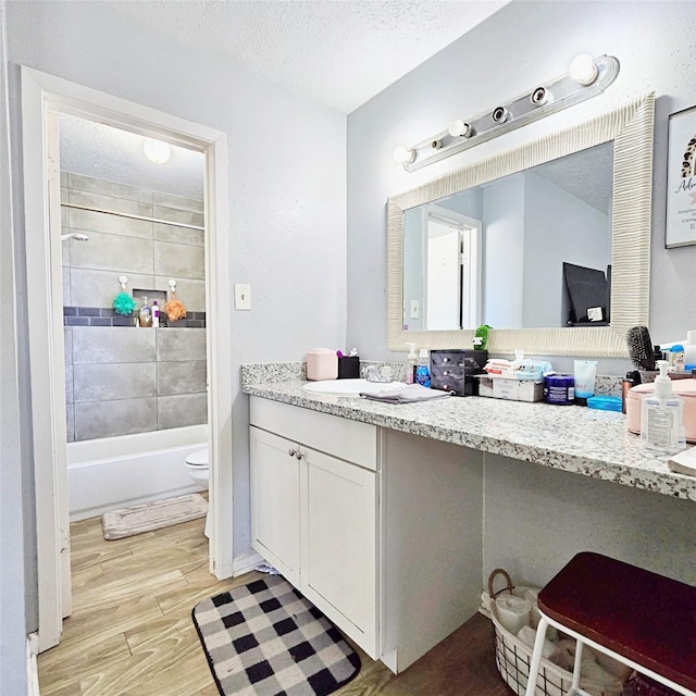 full bathroom with a textured ceiling, toilet, vanity, and tiled shower / bath