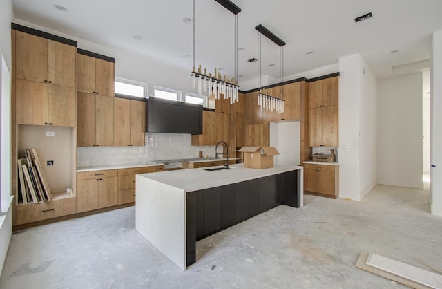 kitchen with a center island with sink, sink, tasteful backsplash, decorative light fixtures, and extractor fan