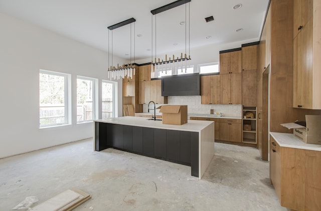 kitchen featuring backsplash, custom range hood, an island with sink, and decorative light fixtures