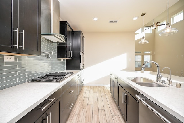 kitchen with tasteful backsplash, stainless steel appliances, sink, wall chimney range hood, and pendant lighting