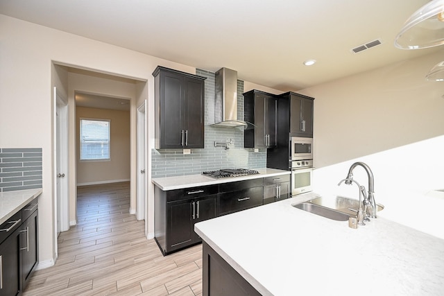 kitchen featuring decorative backsplash, sink, stainless steel appliances, and wall chimney range hood