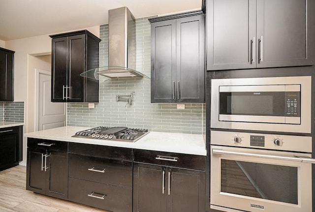 kitchen featuring backsplash, wall chimney range hood, stainless steel appliances, and light hardwood / wood-style flooring