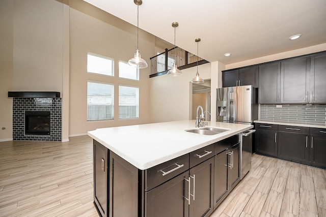 kitchen featuring stainless steel appliances, sink, a tile fireplace, a center island with sink, and hanging light fixtures