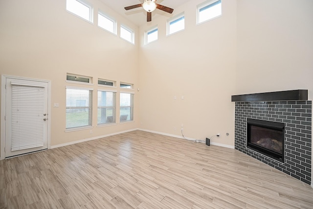 unfurnished living room with ceiling fan, a towering ceiling, a tile fireplace, and light hardwood / wood-style flooring