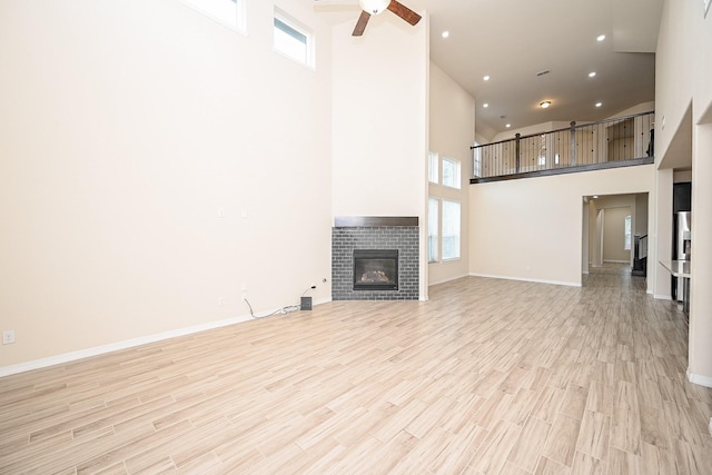 unfurnished living room featuring ceiling fan, light hardwood / wood-style floors, a high ceiling, and a brick fireplace