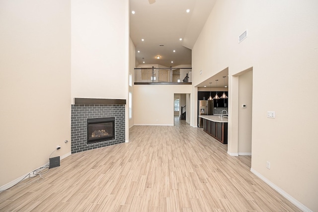 unfurnished living room with sink, a high ceiling, light wood-type flooring, and a tiled fireplace