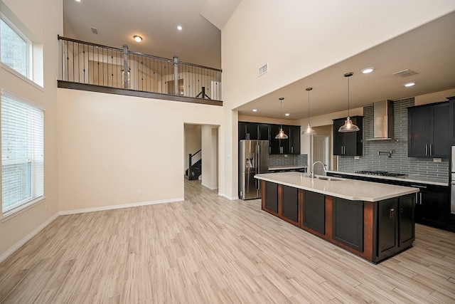 kitchen featuring pendant lighting, backsplash, a kitchen island with sink, wall chimney range hood, and stainless steel appliances