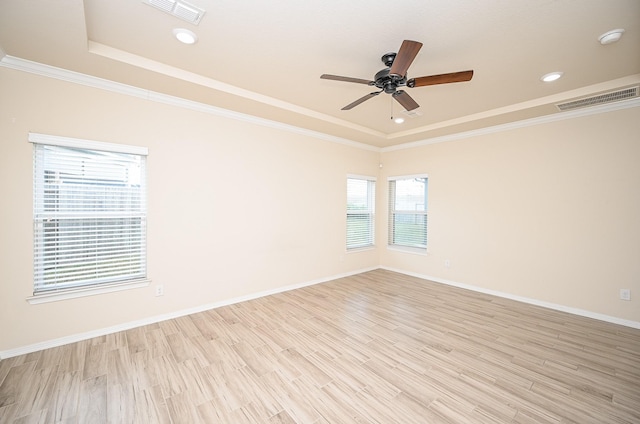 empty room with a raised ceiling, crown molding, ceiling fan, and light wood-type flooring