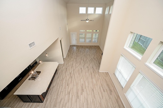 interior space with ceiling fan, light hardwood / wood-style flooring, a towering ceiling, and a healthy amount of sunlight