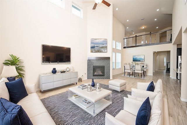 living room featuring ceiling fan, light hardwood / wood-style floors, a high ceiling, and a tiled fireplace