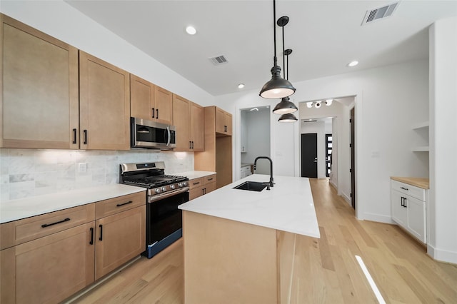 kitchen with sink, stainless steel appliances, tasteful backsplash, decorative light fixtures, and a center island with sink