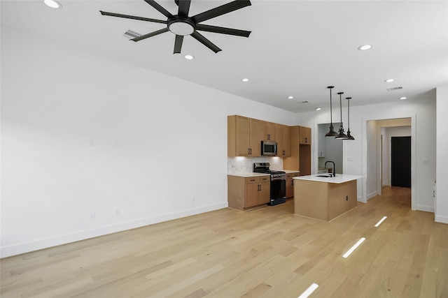 kitchen featuring sink, light wood-type flooring, appliances with stainless steel finishes, pendant lighting, and a kitchen island with sink