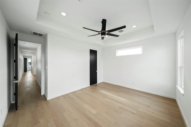 unfurnished room with plenty of natural light, light wood-type flooring, and a tray ceiling