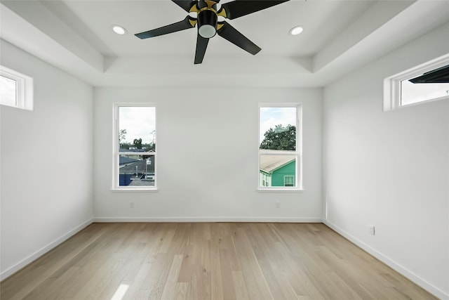 spare room with light hardwood / wood-style floors, a raised ceiling, and ceiling fan