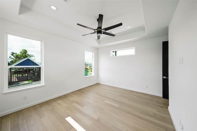 unfurnished room featuring ceiling fan, light wood-type flooring, and a tray ceiling