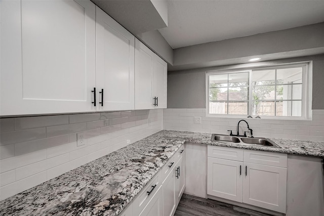 kitchen featuring sink, decorative backsplash, light stone countertops, dark hardwood / wood-style flooring, and white cabinetry