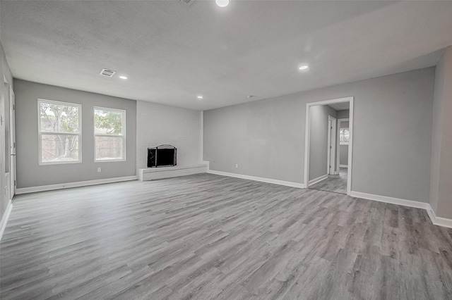 unfurnished living room with a textured ceiling, light wood-type flooring, and a brick fireplace