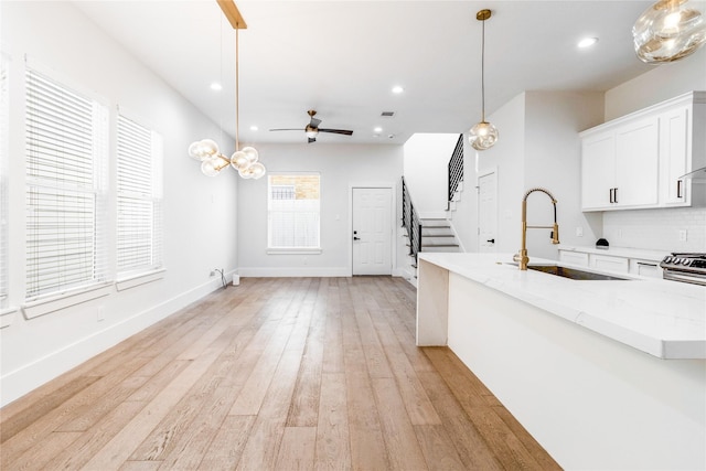 kitchen featuring light wood-type flooring, ceiling fan, sink, white cabinetry, and hanging light fixtures