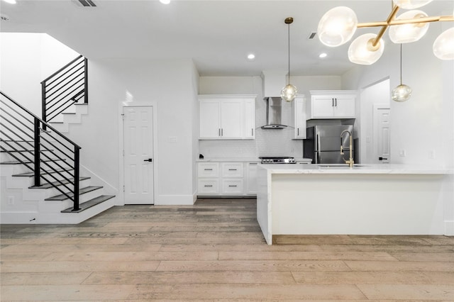 kitchen featuring sink, wall chimney exhaust hood, stainless steel fridge, light wood-type flooring, and white cabinetry