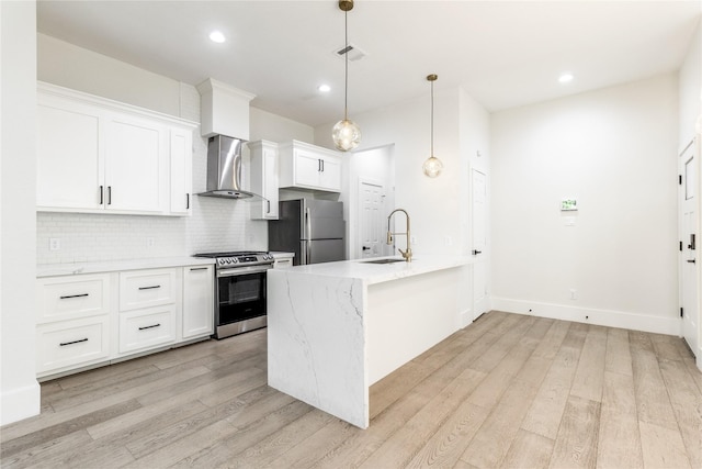 kitchen with white cabinets, wall chimney range hood, sink, light hardwood / wood-style flooring, and appliances with stainless steel finishes