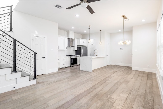 kitchen featuring appliances with stainless steel finishes, light wood-type flooring, wall chimney range hood, pendant lighting, and white cabinetry