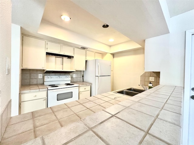 kitchen featuring white appliances, backsplash, sink, a tray ceiling, and tile counters