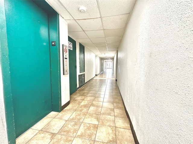 hallway with light tile patterned floors, a paneled ceiling, and elevator