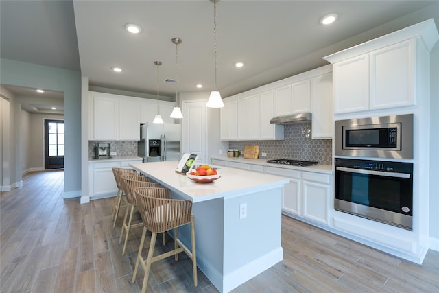 kitchen with white cabinetry, a kitchen breakfast bar, an island with sink, appliances with stainless steel finishes, and light wood-type flooring