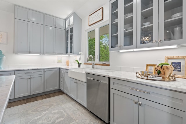 kitchen with stainless steel dishwasher, gray cabinets, light stone counters, and light hardwood / wood-style flooring