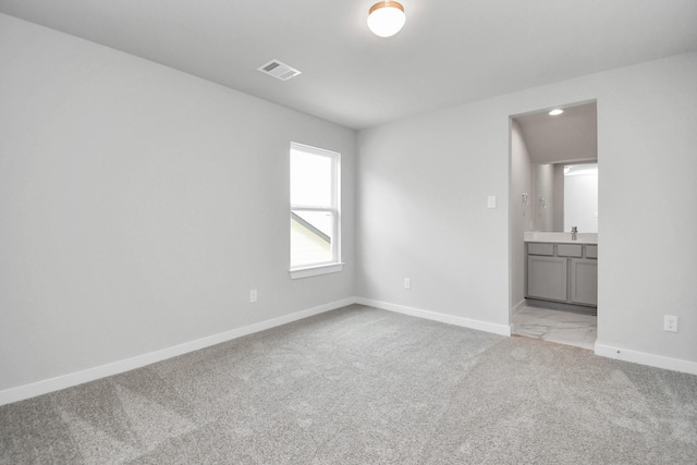 unfurnished bedroom featuring baseboards, ensuite bathroom, visible vents, and light carpet