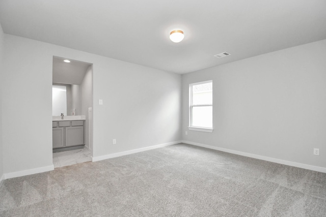 spare room featuring baseboards, light carpet, visible vents, and a sink