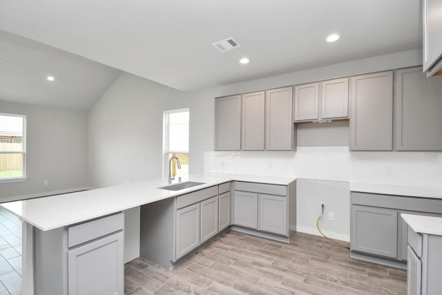 kitchen featuring kitchen peninsula, gray cabinetry, sink, and lofted ceiling