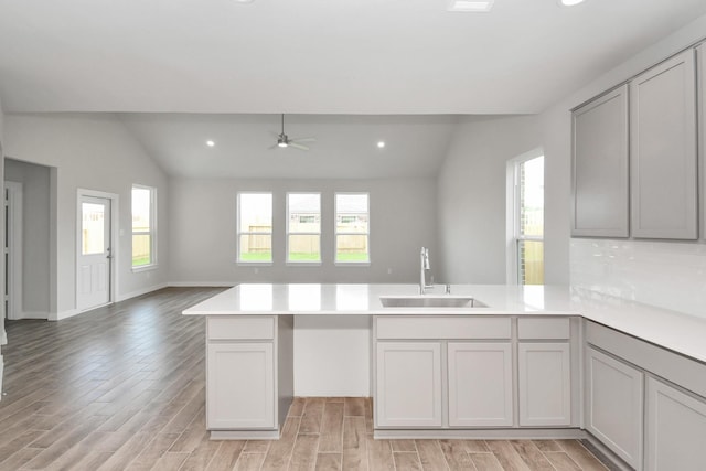 kitchen with sink, vaulted ceiling, ceiling fan, light wood-type flooring, and kitchen peninsula