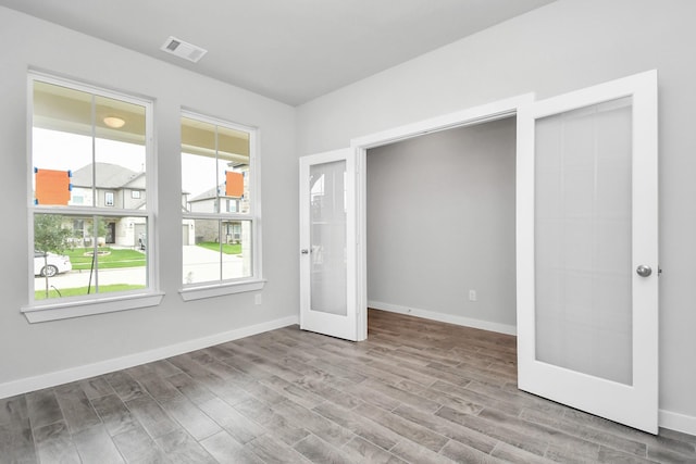 empty room with wood finished floors, visible vents, baseboards, and french doors