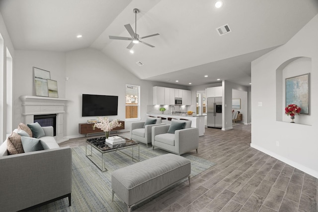 living area featuring baseboards, visible vents, a glass covered fireplace, wood finished floors, and ceiling fan
