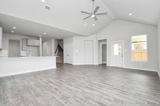 unfurnished living room featuring light wood-type flooring, high vaulted ceiling, ceiling fan, and sink