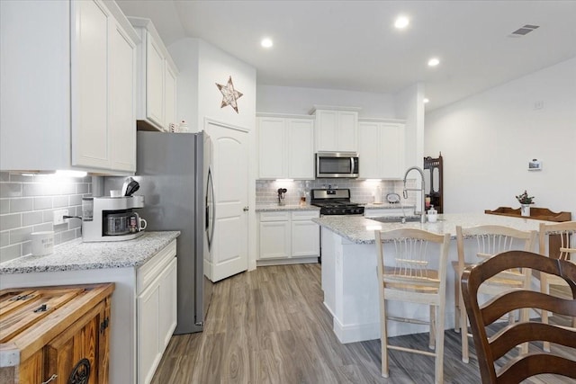 kitchen featuring appliances with stainless steel finishes, tasteful backsplash, sink, light hardwood / wood-style flooring, and white cabinetry