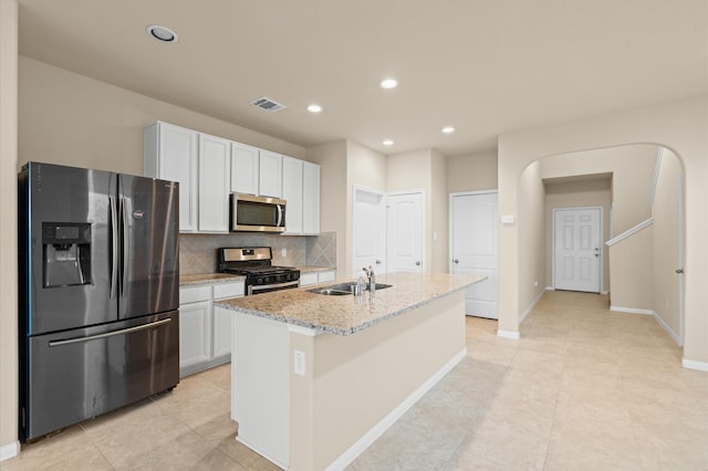 kitchen featuring a kitchen island with sink, sink, light stone countertops, appliances with stainless steel finishes, and white cabinetry