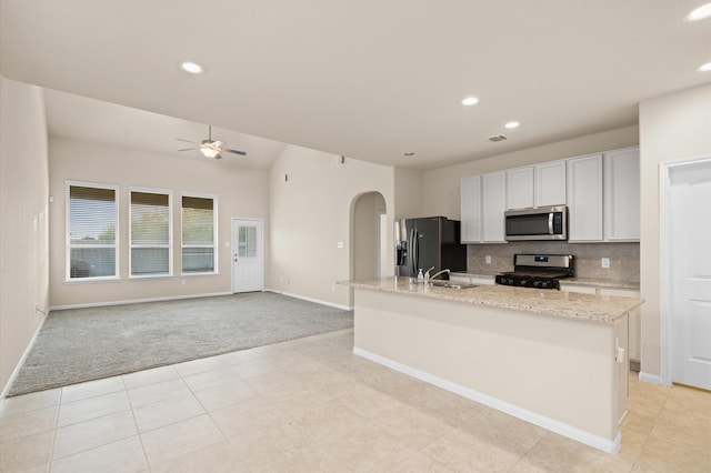 kitchen with white cabinetry, stainless steel appliances, light stone counters, light colored carpet, and a center island with sink