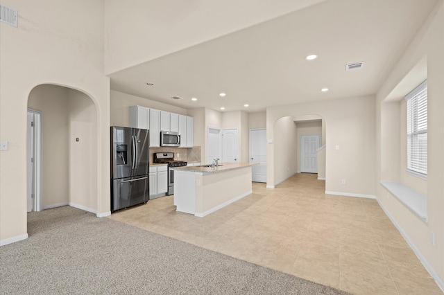 kitchen featuring white cabinetry, light stone countertops, light colored carpet, a kitchen island with sink, and appliances with stainless steel finishes