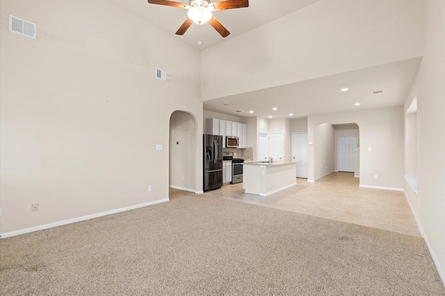 unfurnished living room with ceiling fan, light colored carpet, a towering ceiling, and sink