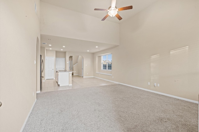 unfurnished living room featuring light carpet, high vaulted ceiling, and ceiling fan