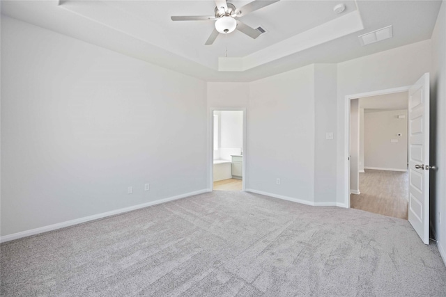 unfurnished bedroom featuring light carpet, connected bathroom, a raised ceiling, and ceiling fan