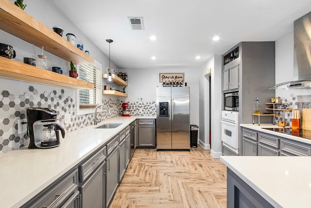 kitchen featuring sink, stainless steel appliances, wall chimney range hood, pendant lighting, and gray cabinets