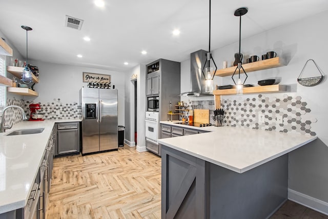 kitchen featuring kitchen peninsula, appliances with stainless steel finishes, wall chimney exhaust hood, sink, and pendant lighting