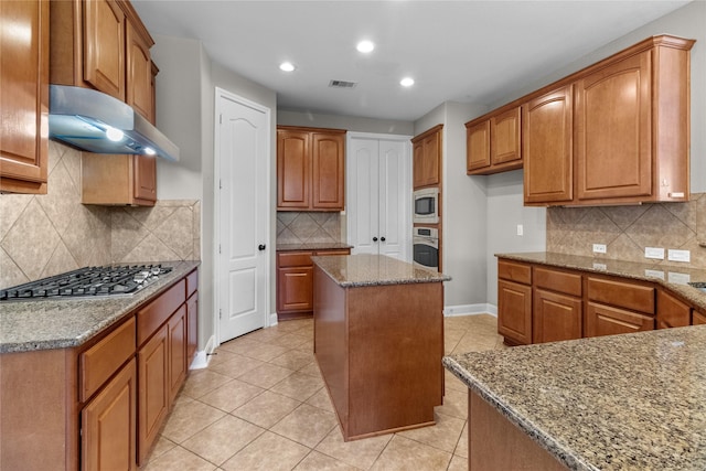 kitchen featuring a kitchen island, stone countertops, decorative backsplash, light tile patterned floors, and appliances with stainless steel finishes